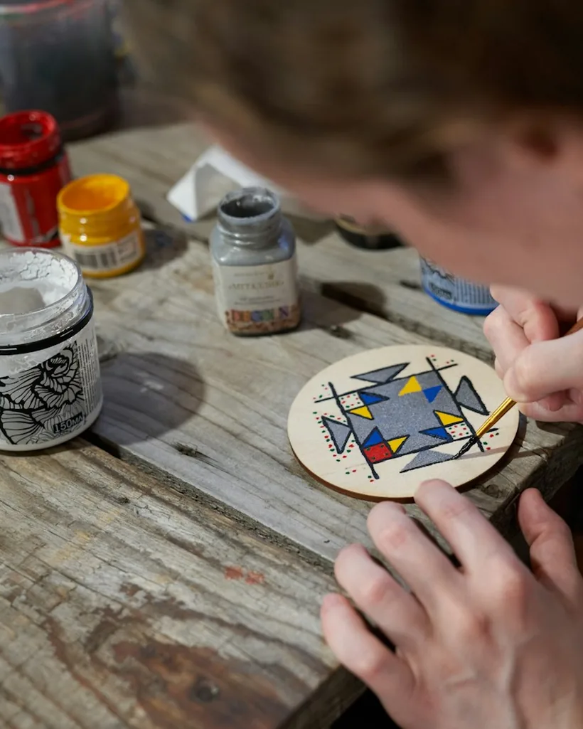 Detalle de un pincel trazando un motivo decorativo de colores sobre una pieza pequeña de fondo oscuro